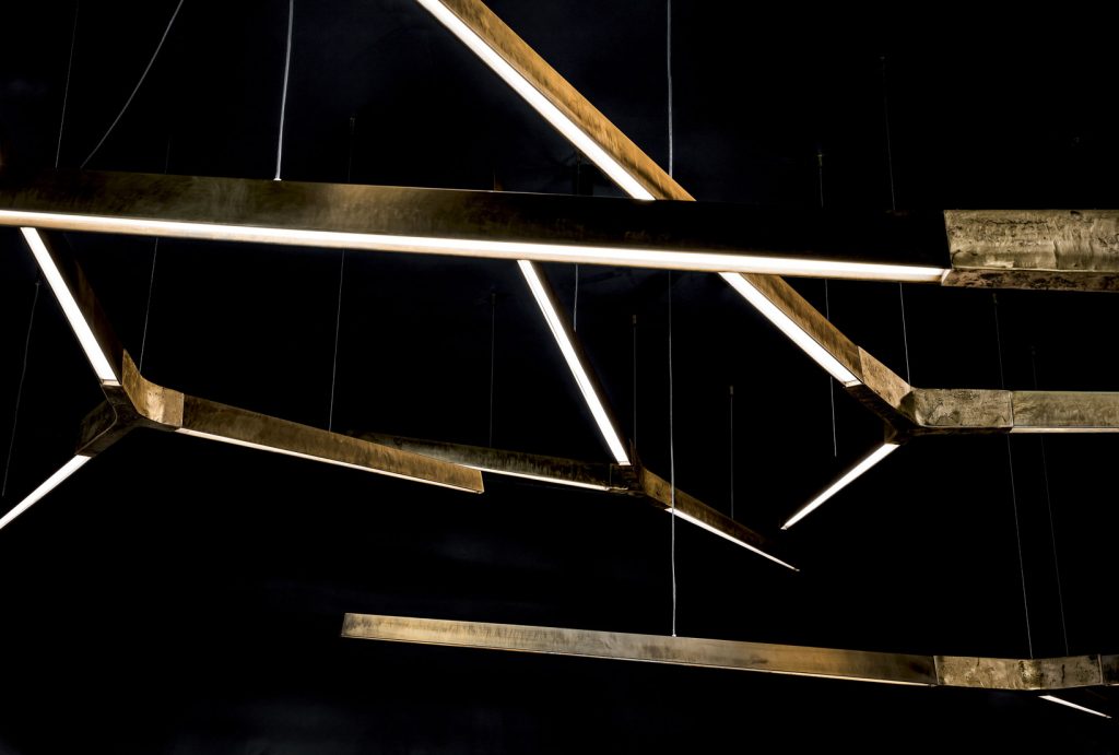 Three Starlight Horizontal led lamps with with Y shaped central body in sandcasting brass using suspension cables on a black background.