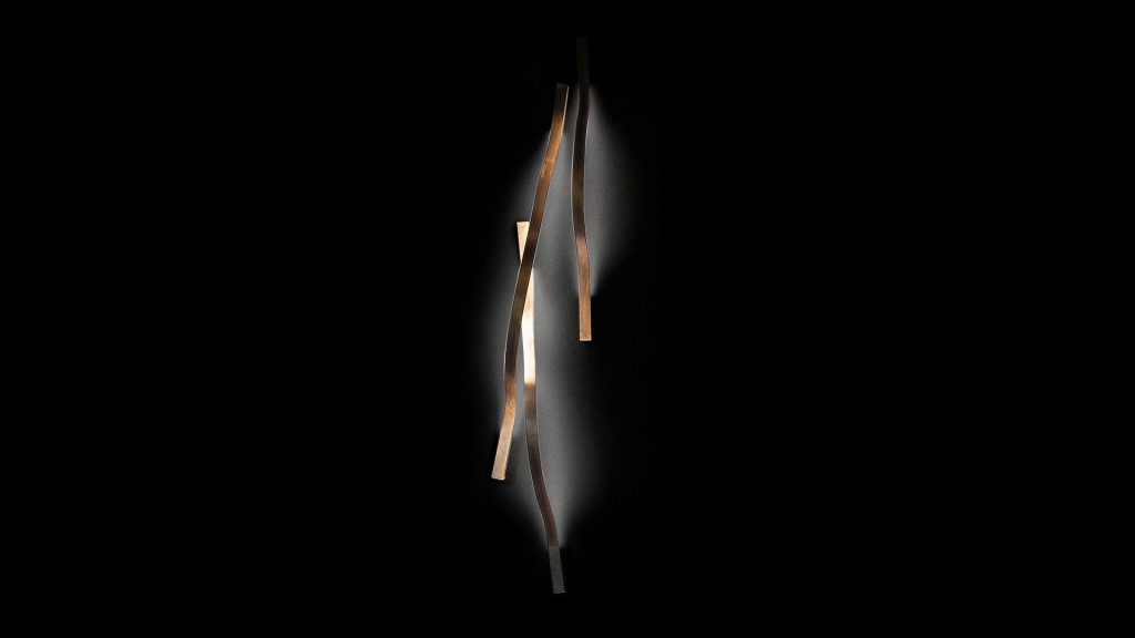 wall lamp made of burnished brass with a curved design on a black background