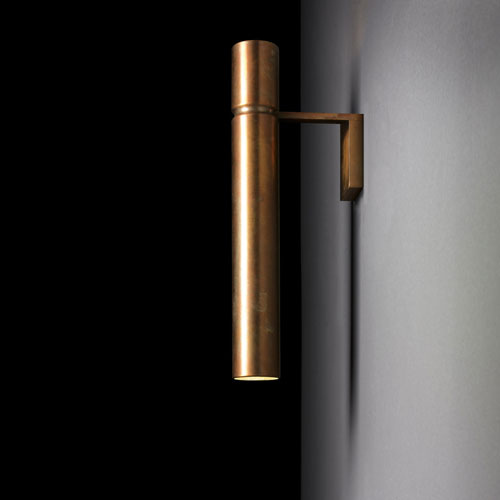 Ceiling Tubular Light with a cylindrical shape in bronze attached to a black wall with a bronze support.