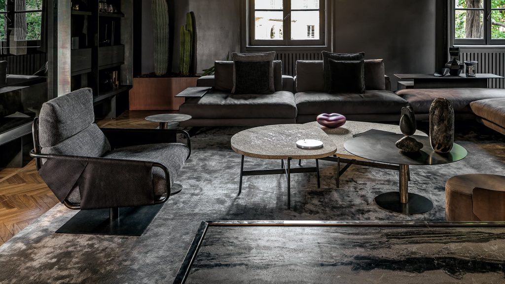 Voyage armchair, curved bronze steel structure with brown leather, gray leather cushion upholstery, central black steel leg in a living room.