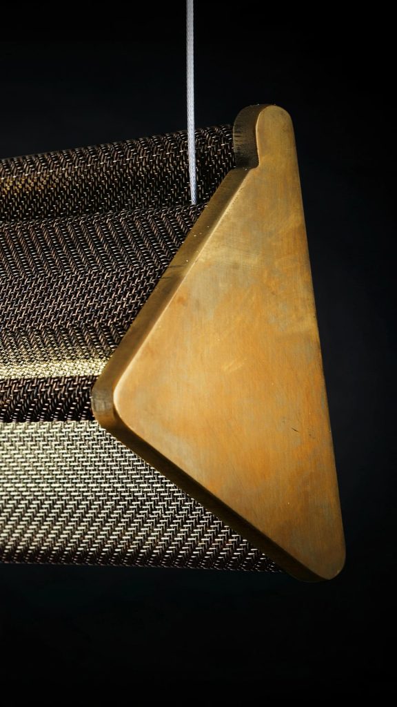 Closedup of Y Light of Y shaped body with steel suspension cables. Finish structure in brass on a black background.