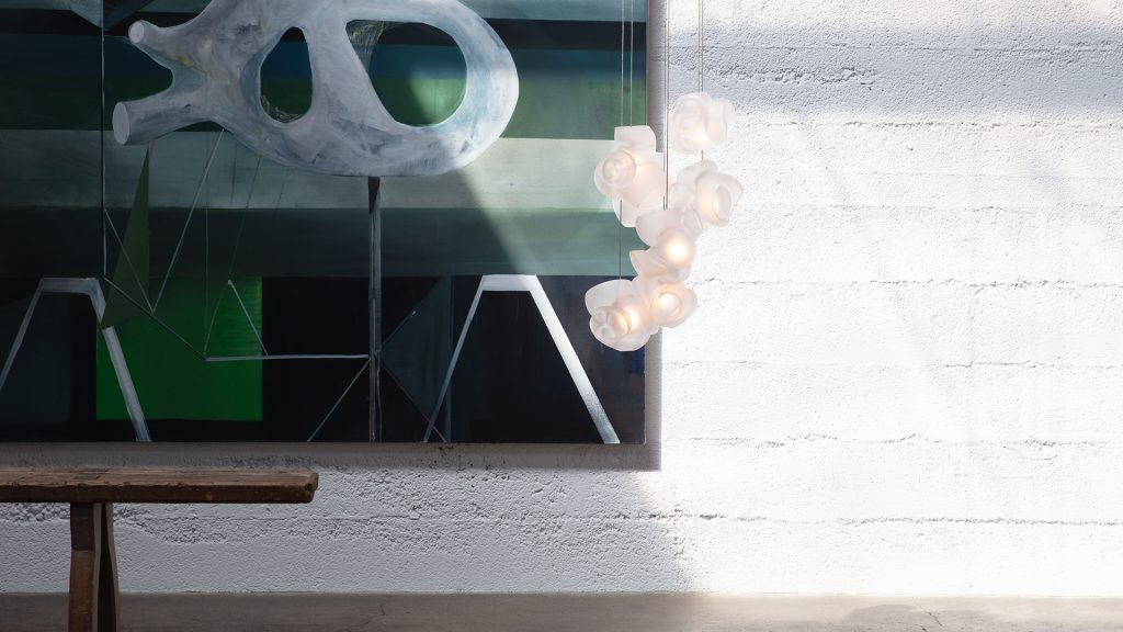 One Hundred Clear light illuminated hanging from the ceiling in front of an art work on the wall