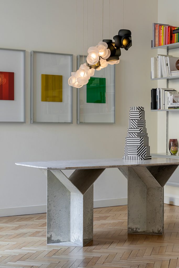 One Hundred Clear with Gray light haning over a grey table and three art pieces hanging on the wall in the background