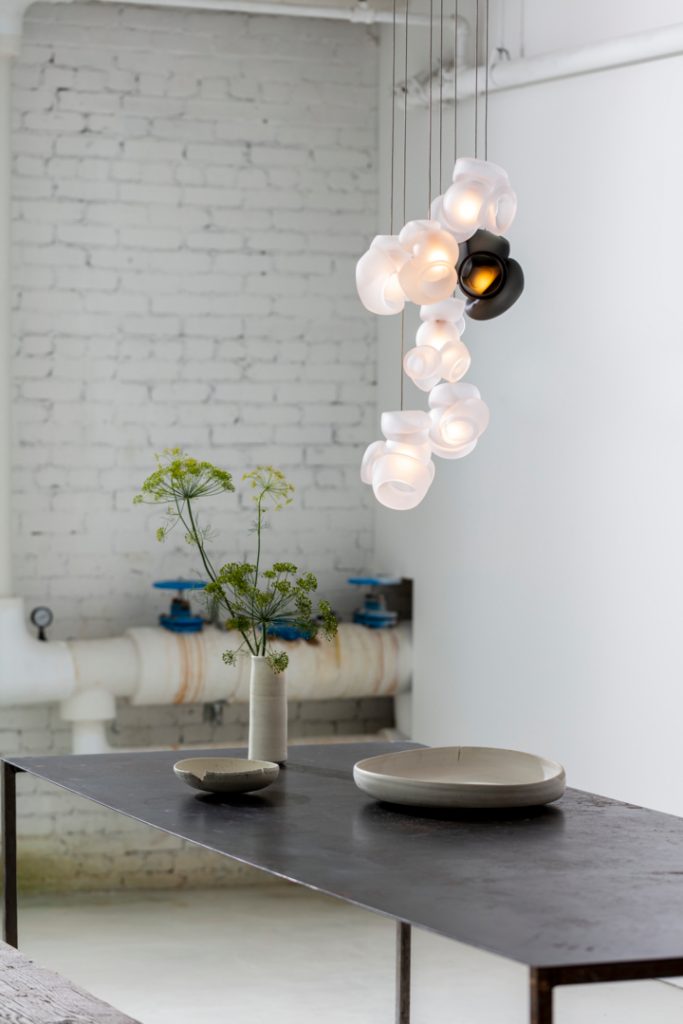 One Hundred Clear with Gray light hanging illuminated in a white walled room with a table underneath