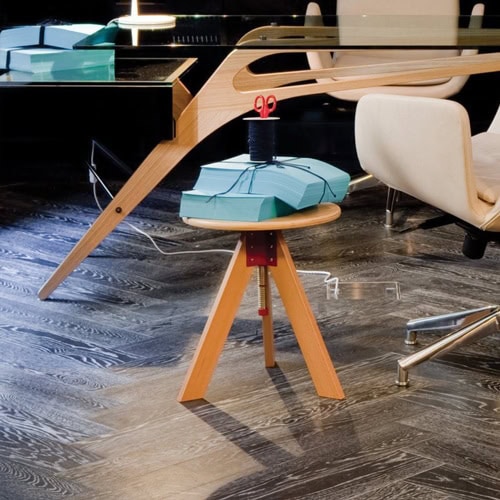 Giotto stool, round top and three legs in natural wood color next to a table.