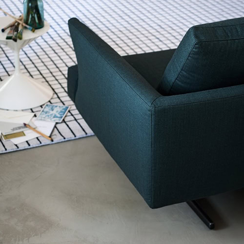 Closeup of Hiro sifa with backrest and armrest in green fabric and four black legs in a living room.