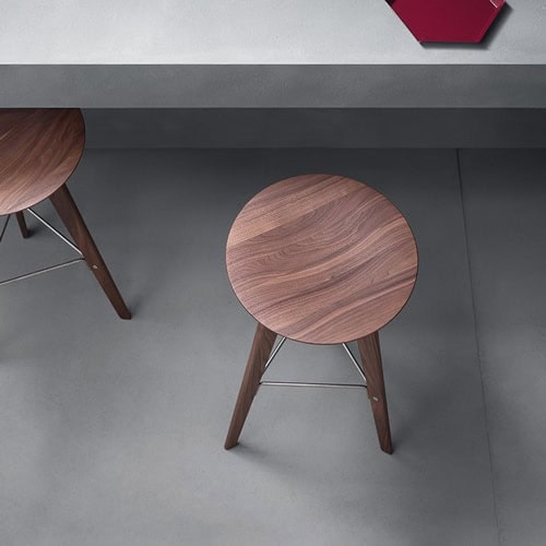 Two Ido chairs made of wood with a round top and four legs united by metal rods under a table.