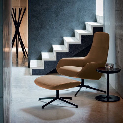 Kent armchair with footrest featuring a brown padded seat and backrest and slender black metal leg in a living room.