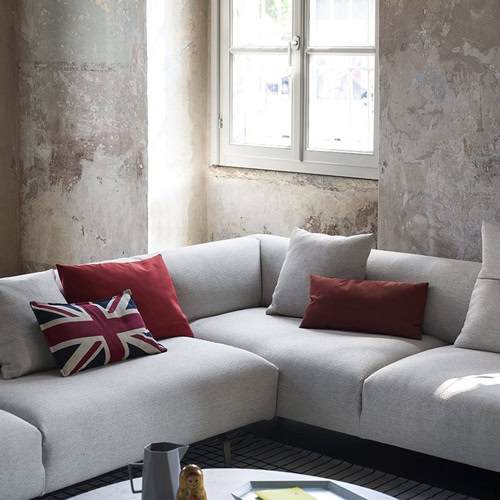 L shaped Kim sofa featuring steel legs and an upholstered seat and backrest in gray fabric in a living room.