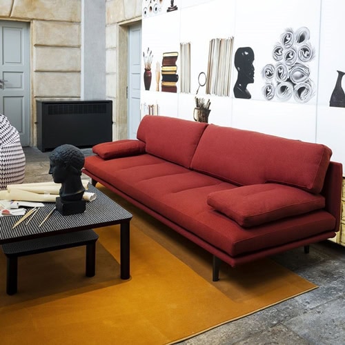 Red Milano+ sofa with armrest and backrest and a black metal frame in a living room.
