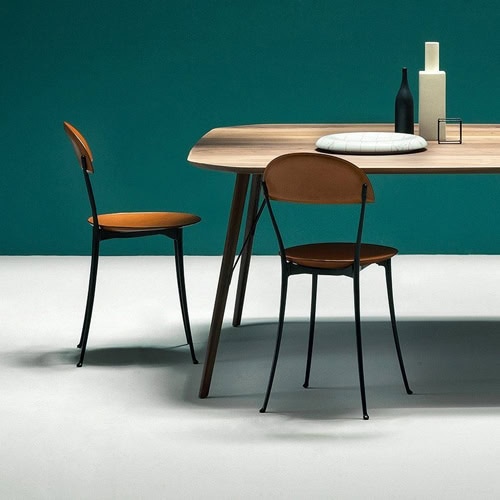 Two Tonietta chairs featuring a orange cushioned seat and backrest, and black metal frame in a dining room.