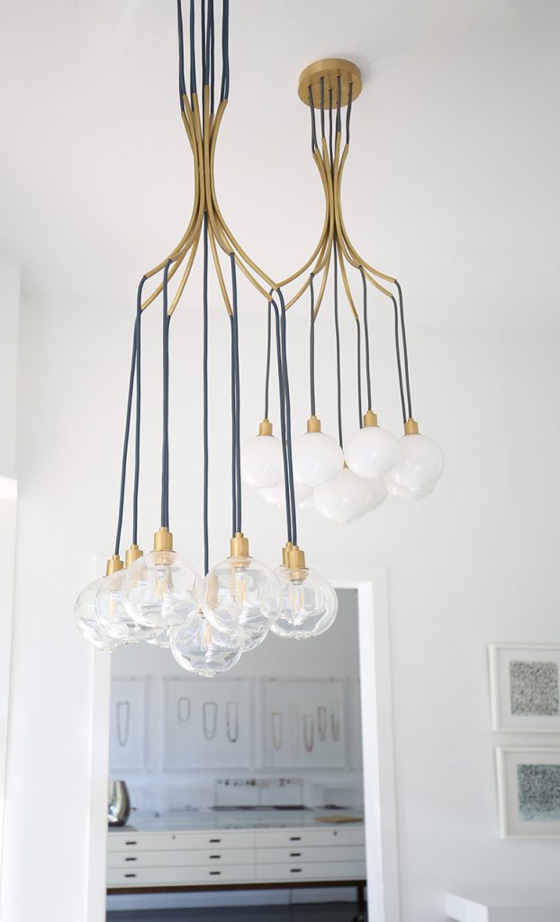 Drape chandelier in transparent glass and gold base with LED lighting on a white background.
