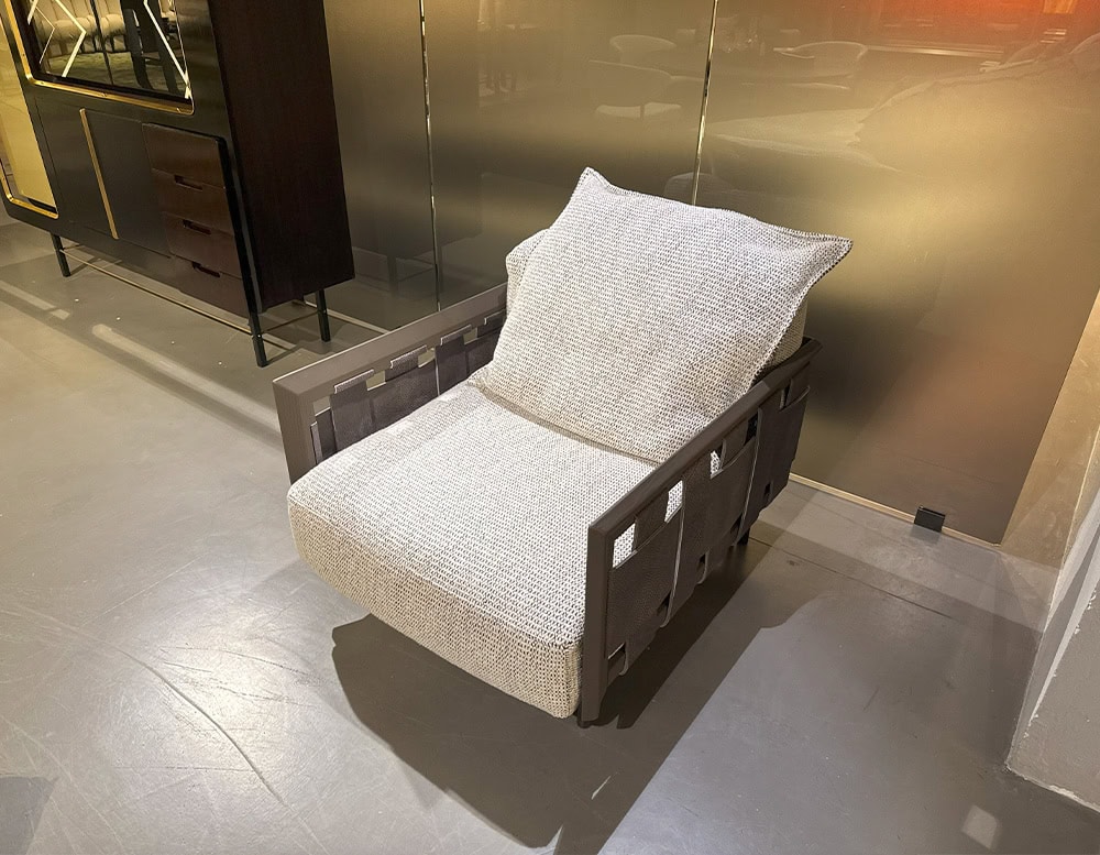 Hen Armchair RF features wide woven sides and a substantial cushion in soft beige upholstery. A relaxed lounge piece with a grounded silhouette and earthy tones, ideal for casual elegance.