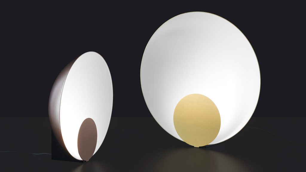 hemispherical table lamp with a disc on its front made of metal in a gold and brown tone in an black background