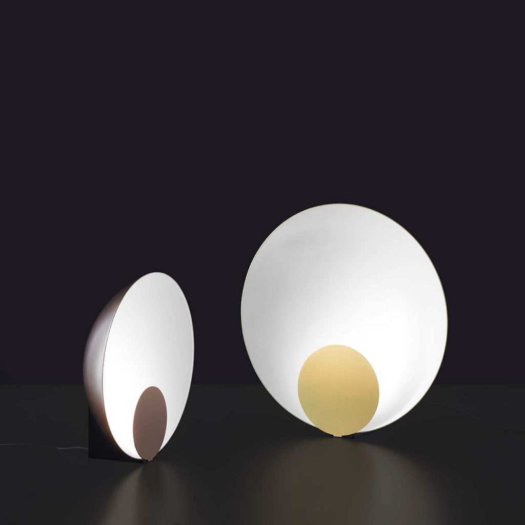 hemispherical table lamp with a disc on its front made of metal in a gold and brown tone in an black background