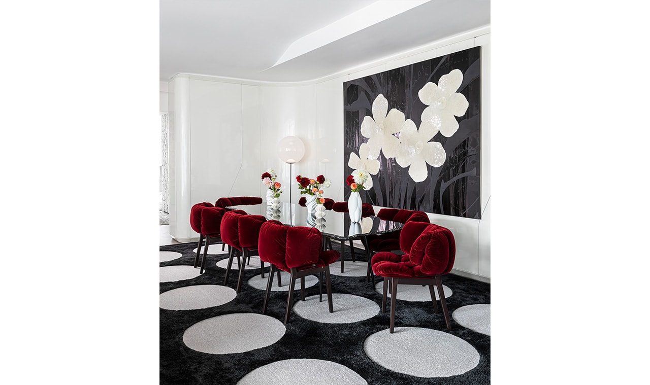 A modern dining room featuring bold red velvet chairs, a black and white geometric rug, and a striking floral wall art piece, creating a sophisticated and stylish space