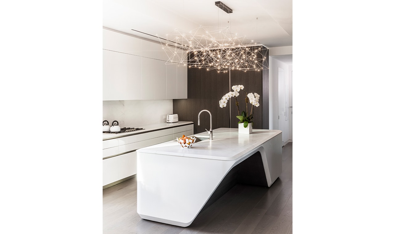 A sleek, modern kitchen featuring a sculptural white island, minimalist cabinetry, and a statement chandelier with delicate glass elements, creating a luxurious atmosphere