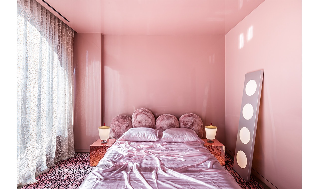 A cozy bedroom with soft pink walls, a plush pink bed, and warm ambient lighting from bedside lamps, creating a serene and inviting atmosphere