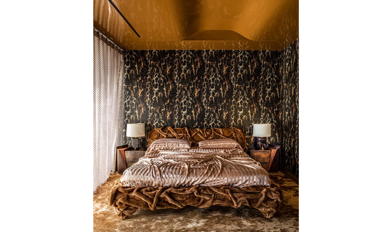 A luxurious bedroom featuring rich earth tones, an opulent patterned bedspread, and ambient lighting from matching bedside lamps, creating a warm and inviting space