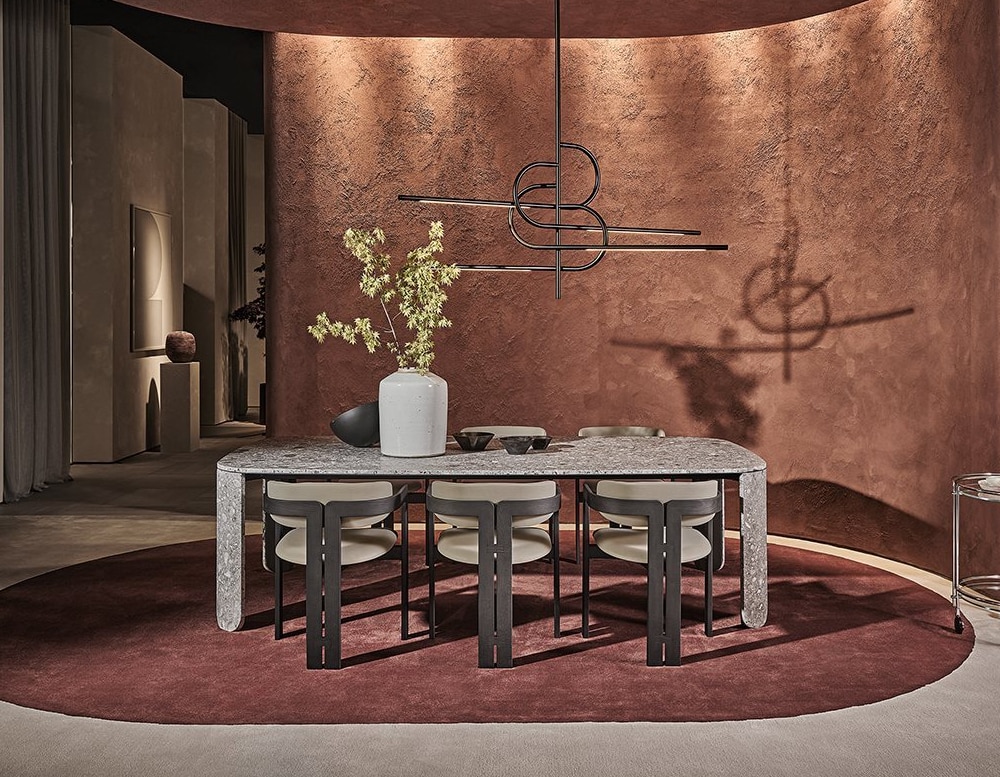 Clemo table with chairs in front of the table, a plant on top of the table, a chandelier hanging above, and a pink wall in the background