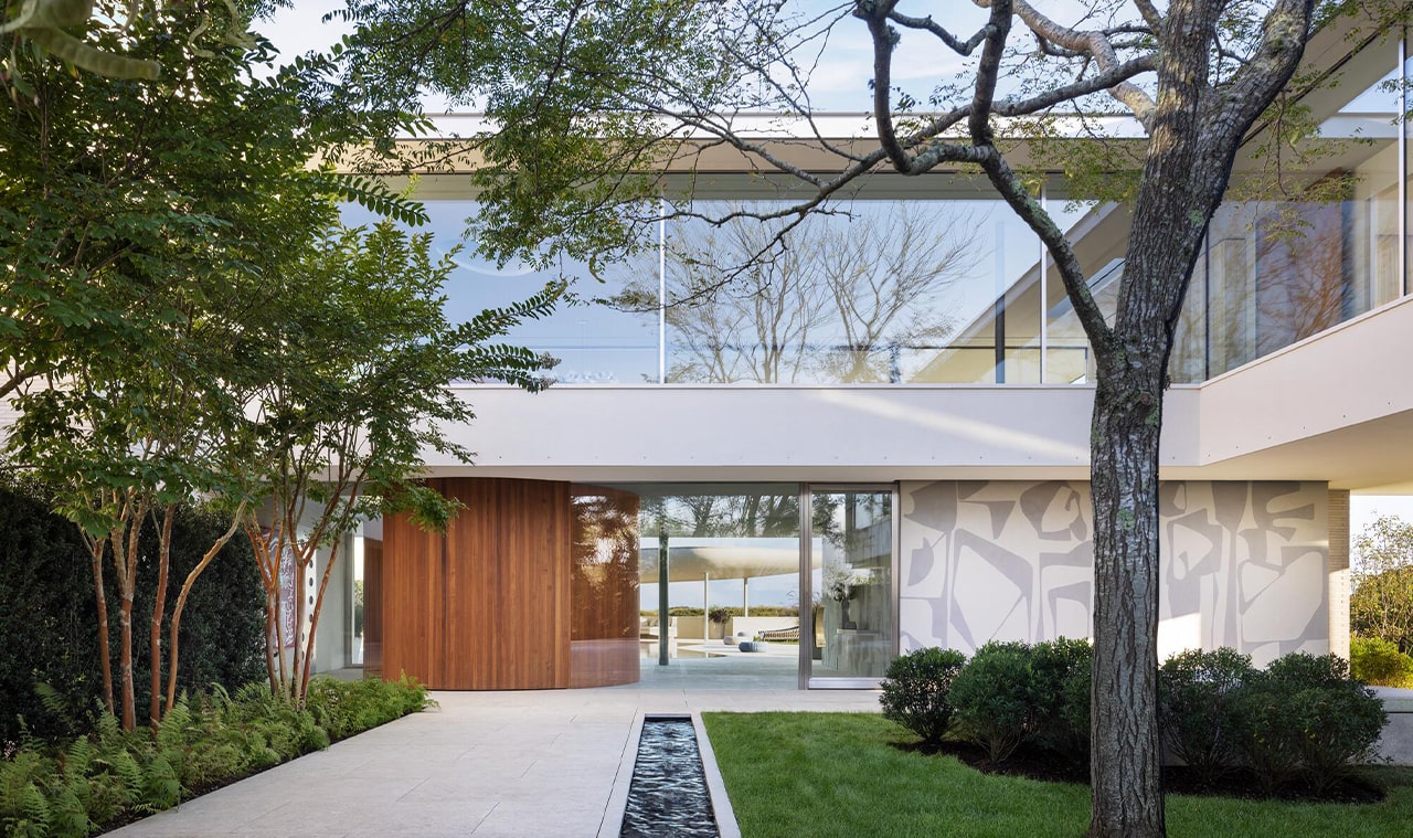 A modern home exterior with floor-to-ceiling glass windows, wooden accents, and a landscaped pathway leading to the entrance