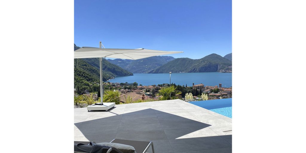 A luxurious infinity pool with the Spectra Umbrosa shade overlooking a stunning mountain lake view, creating a serene and stylish outdoor escape