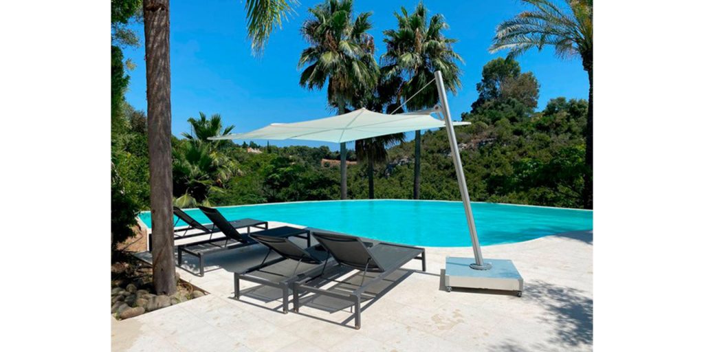A tropical poolside retreat with the Spectra Umbrosa shade, sleek lounge chairs, and lush palm trees, creating a relaxing and stylish outdoor oasis