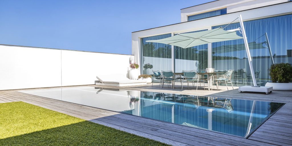 A modern outdoor space featuring the Spectra Umbrosa shade, a sleek infinity pool, and minimalist lounge seating, all set against a bright blue sky