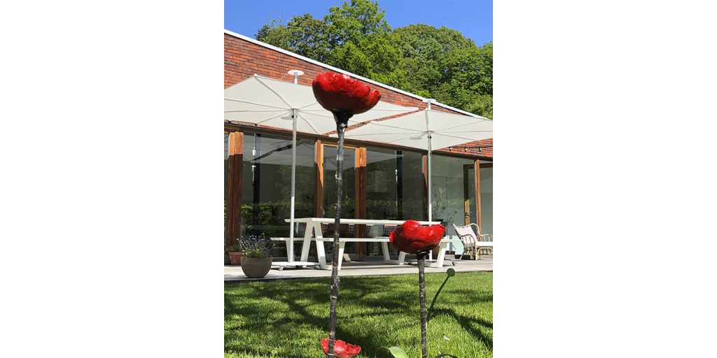 A modern outdoor space featuring a minimalist shade structure over a white dining set, with vibrant red garden sculptures adding a bold artistic touch