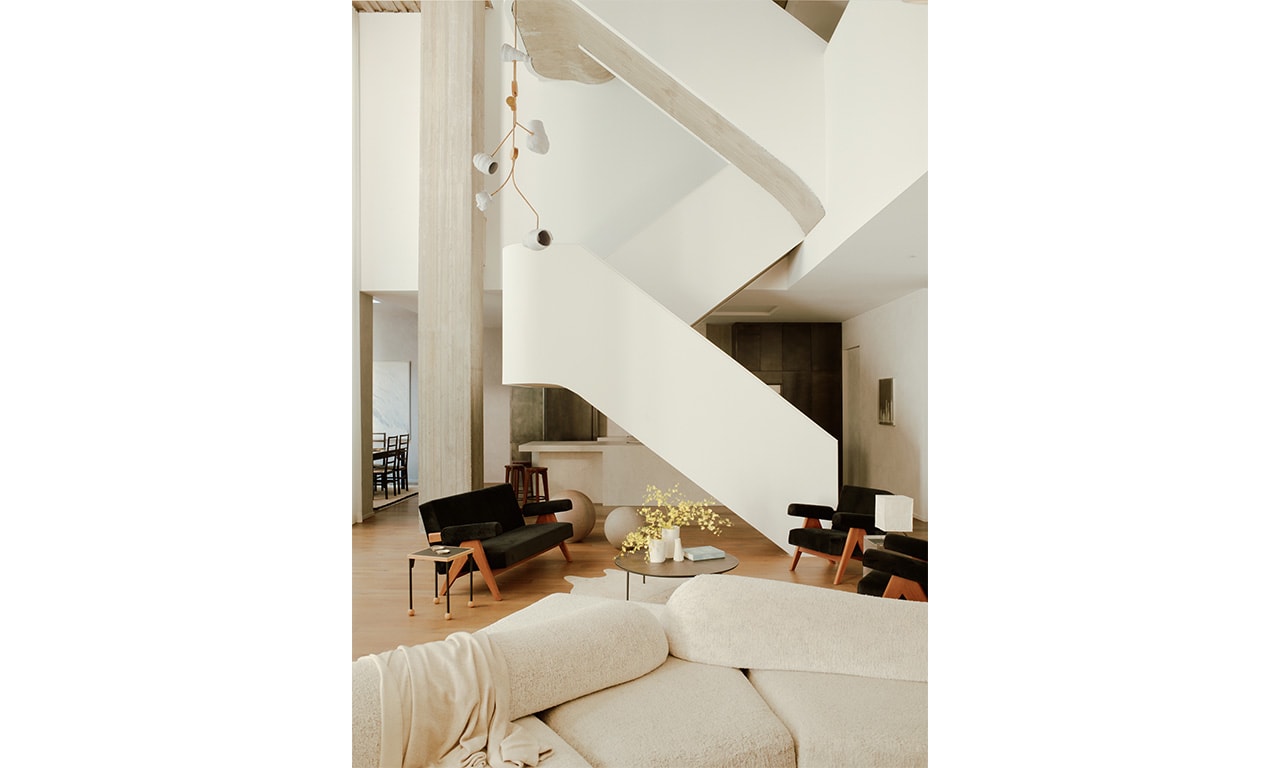A contemporary living area with a sculptural white staircase, plush neutral seating, and black accent chairs, creating a striking contrast in a light-filled space