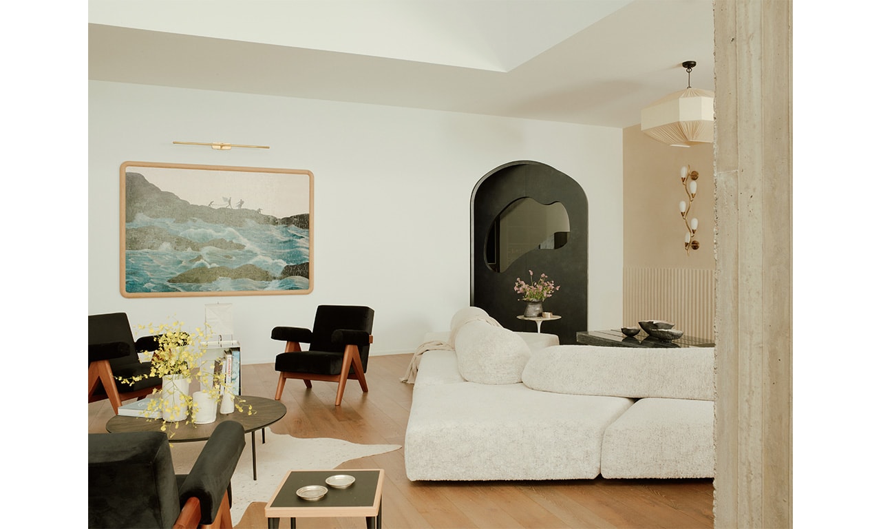 A serene living space with neutral tones, a plush sectional sofa, and a bold black accent chair, complemented by soft lighting and a statement arched doorway