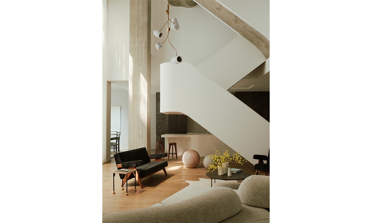 A contemporary living space with an angular staircase as a focal point, complemented by minimalist furniture, warm wood flooring, and natural light filtering through large windows