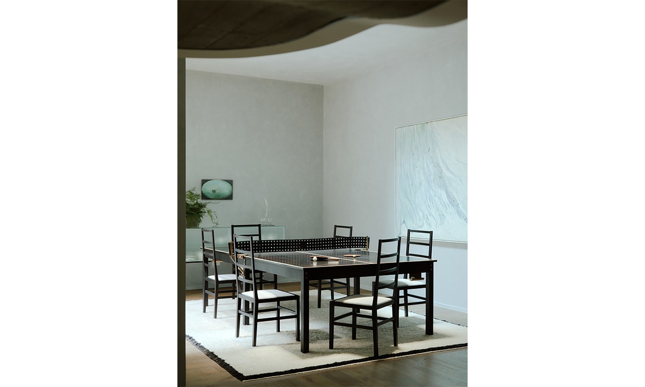 A contemporary dining space featuring a striking black table with matching chairs, set against a minimalist backdrop with soft lighting and organic architectural details