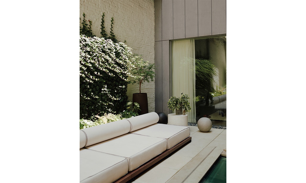 A modern outdoor lounge with sleek, cushioned seating, surrounded by lush greenery and a calming water feature, creating a peaceful retreat