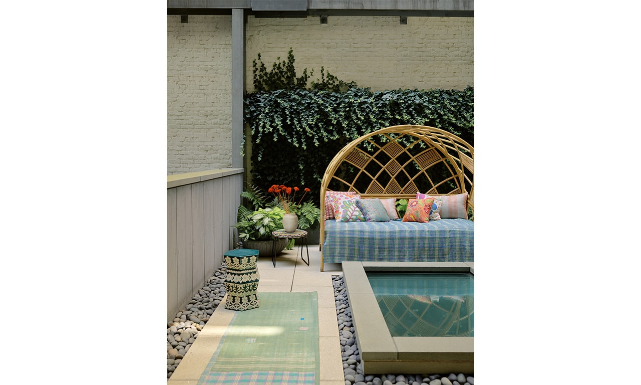 A serene outdoor retreat featuring a stylish rattan daybed adorned with patterned cushions, a tranquil water feature, and lush greenery enhancing the relaxing ambiance