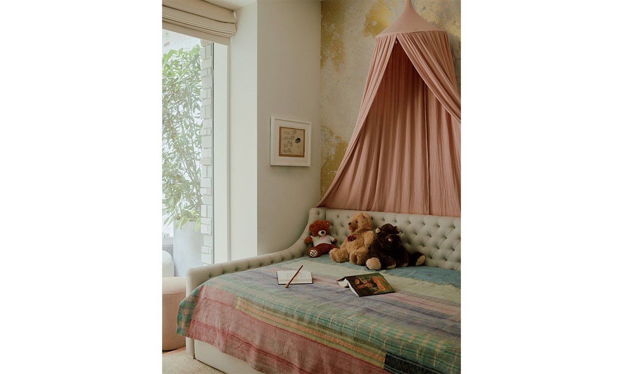 A cozy and charming bedroom featuring a daybed with a pastel patchwork quilt, a soft pink canopy, and plush toys adding a whimsical touch