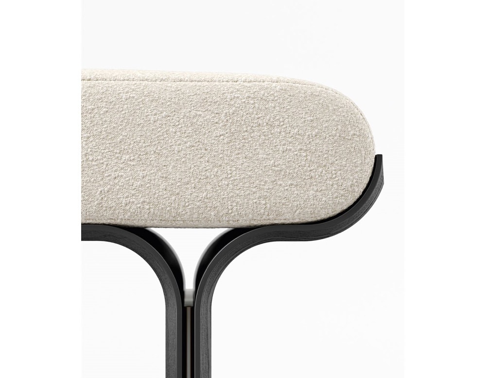 Side of a bench with curved black stained ash base and bright brass details with a cushion covered by white fabric