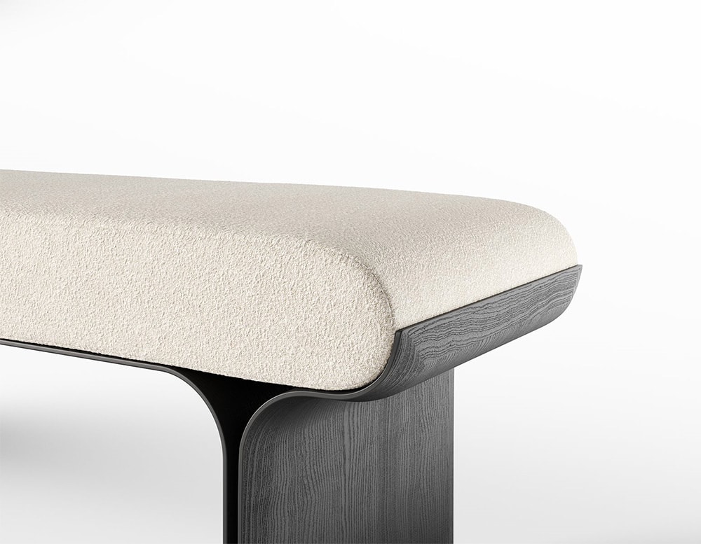 Side of a bench with curved black stained ash base and bright brass details with a cushion covered by white fabric