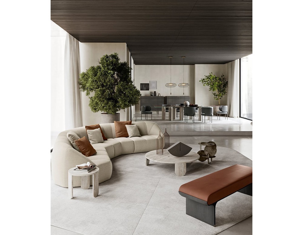 Bench with curved black stained ash base and bright brass details with a cushion covered by brown leather in a living room next to a white sectional