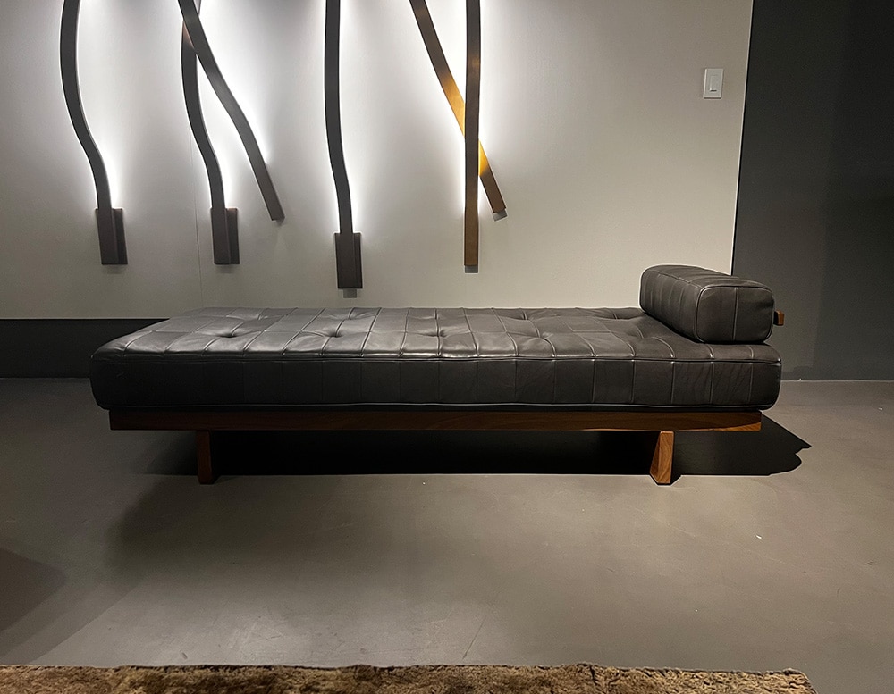 Daybed of black leather atop a frame made of filigree wood slats of brown color