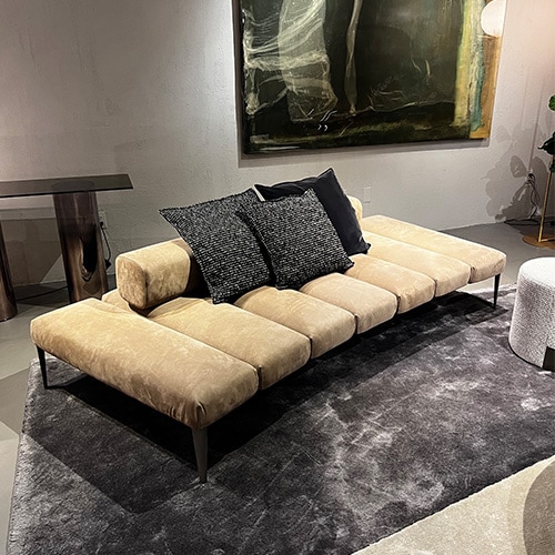 Sofa with backrest covered in beige leather with 7 divisions, thin black legs and black decorative cushions