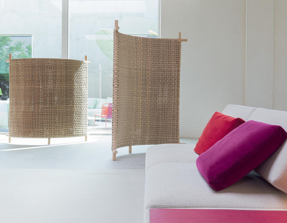 Wood-colored curved screen made of natural sassafras heartwood with plastic spacers in a room next to a white sofa with fuchsia cushions