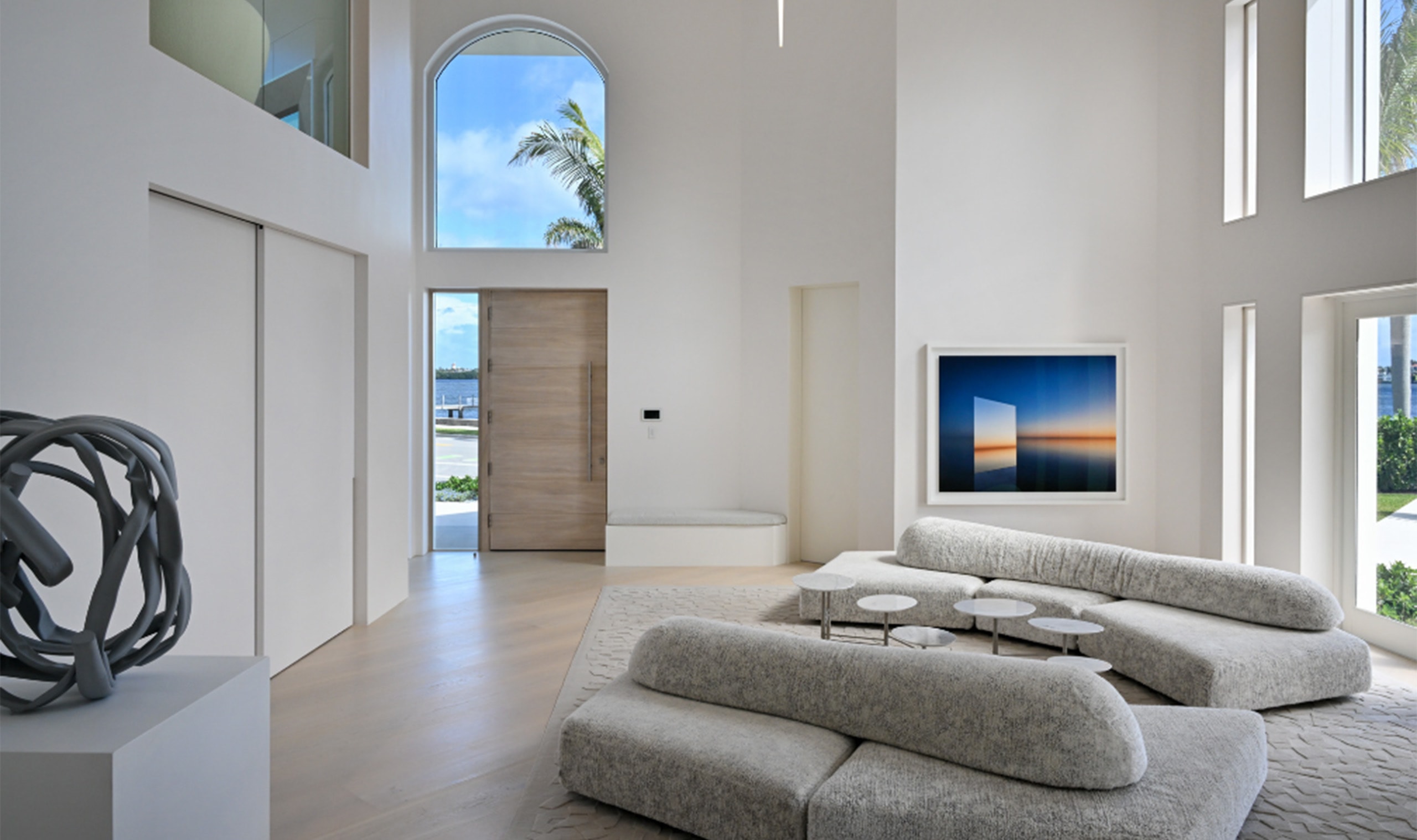 A serene living space with minimalist furnishings, high ceilings, and natural light pouring in through arched windows and open doors