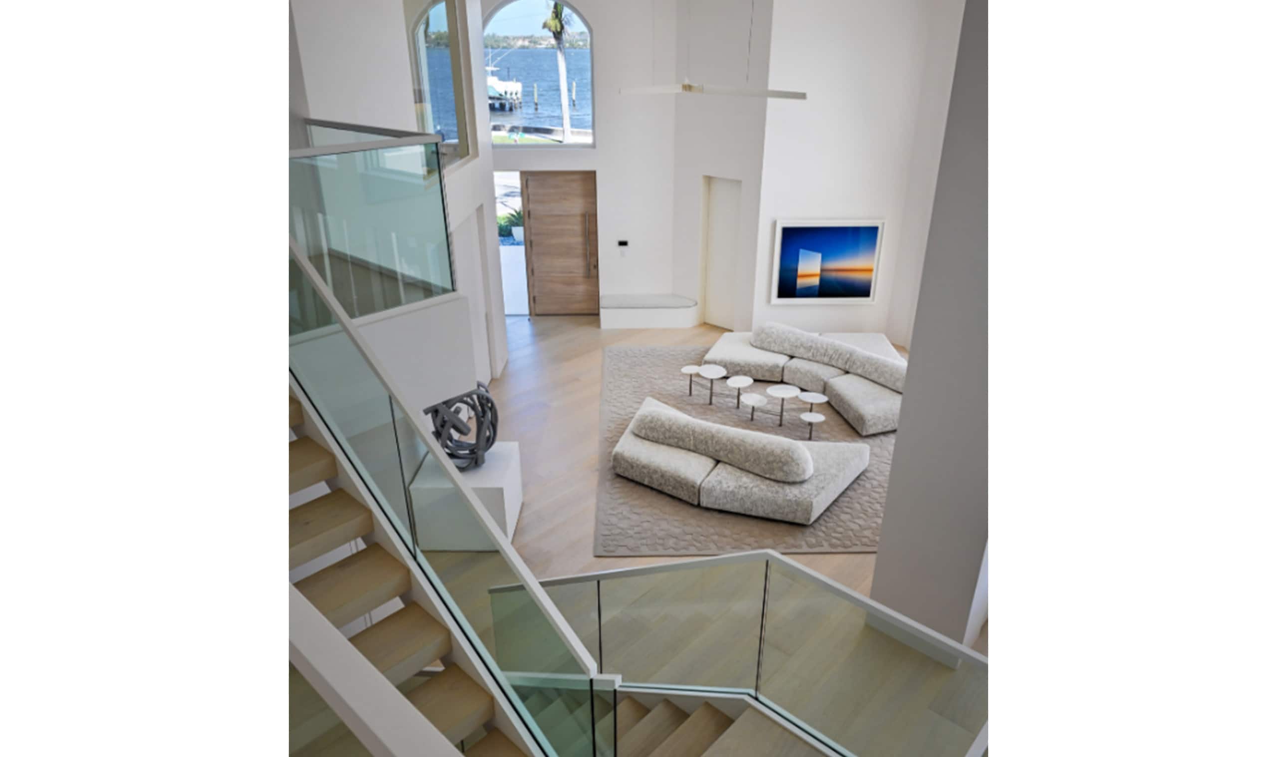 A modern living space with soaring ceilings, a curved glass staircase, and a plush white sectional creating a sophisticated yet inviting ambiance