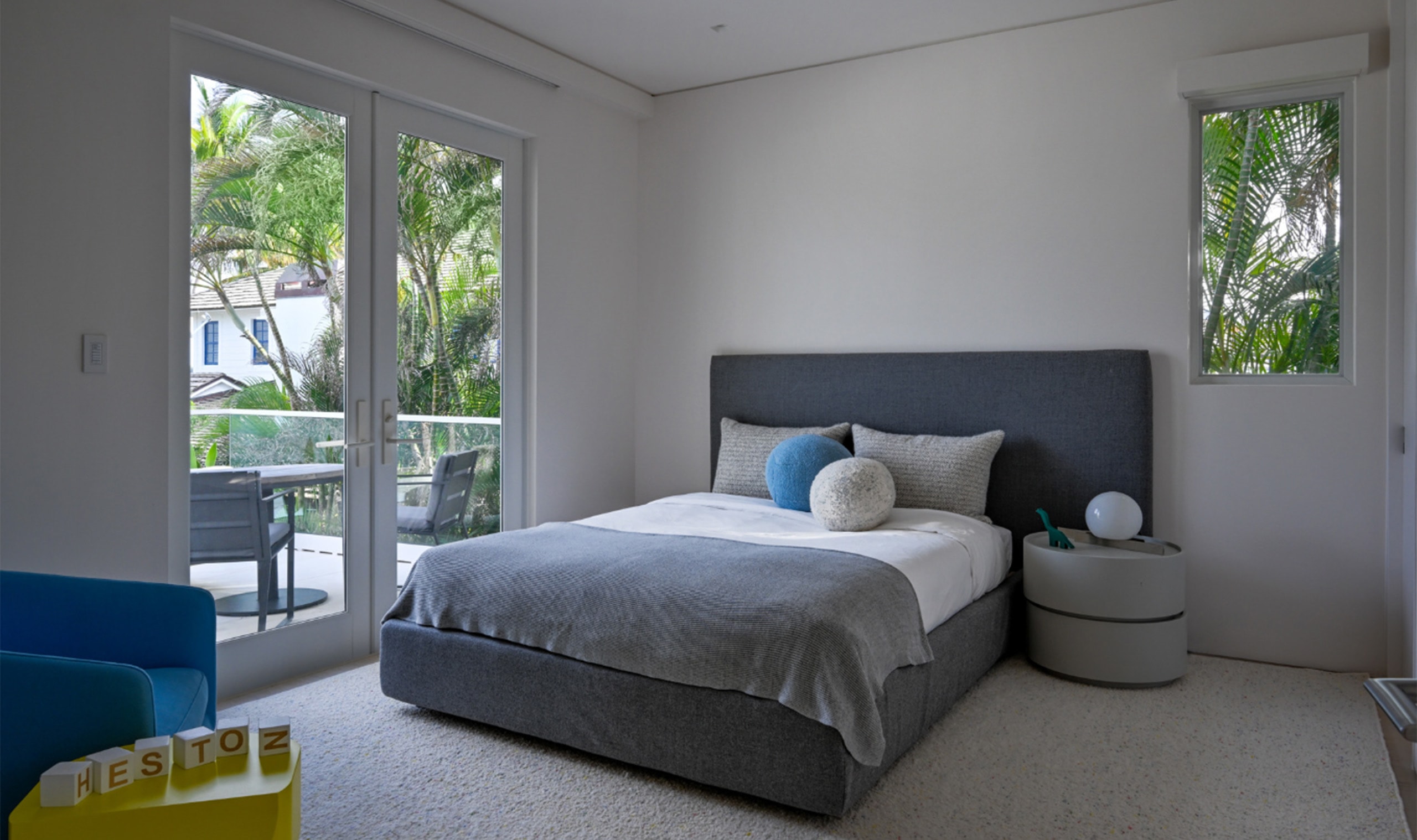 A serene bedroom with a plush upholstered bed, soft neutral bedding, and a cozy ambiance complemented by natural light from glass doors