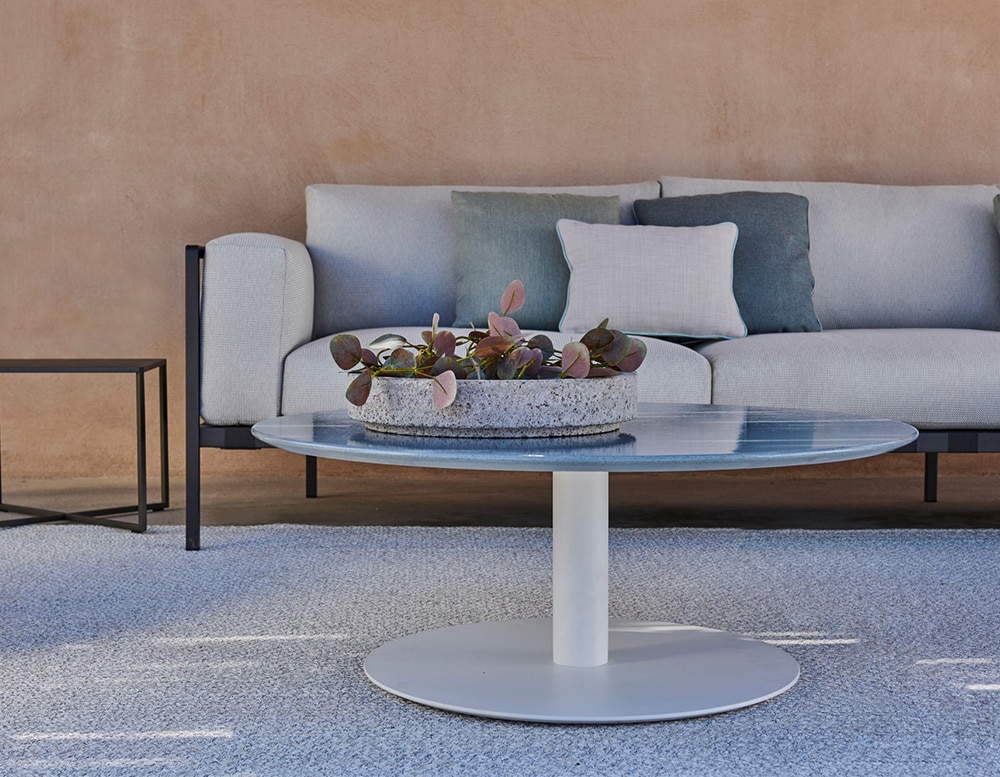 A modern outdoor seating area with a sleek sofa, soft blue cushions, and a minimalist round coffee table on a textured rug