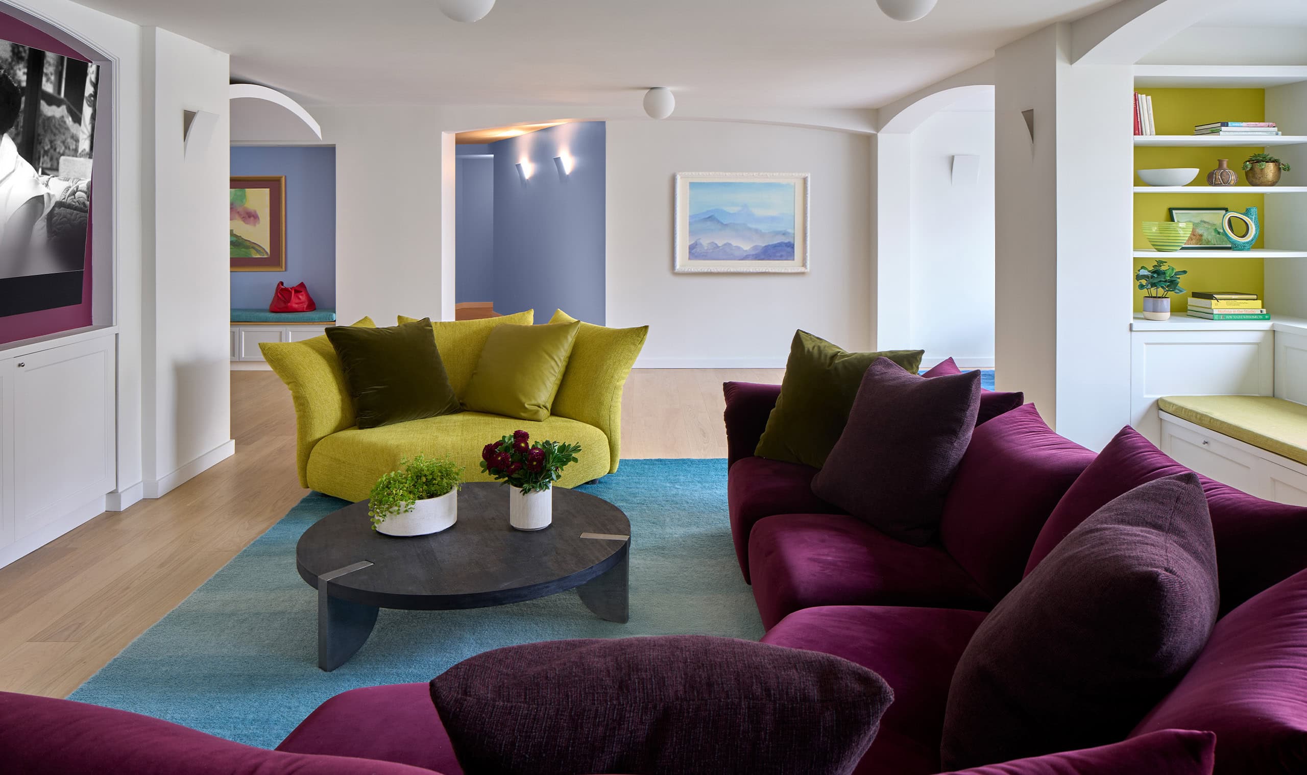 A stylish living room with bold purple and green seating, a round stone coffee table, and a bright open space with modern decor