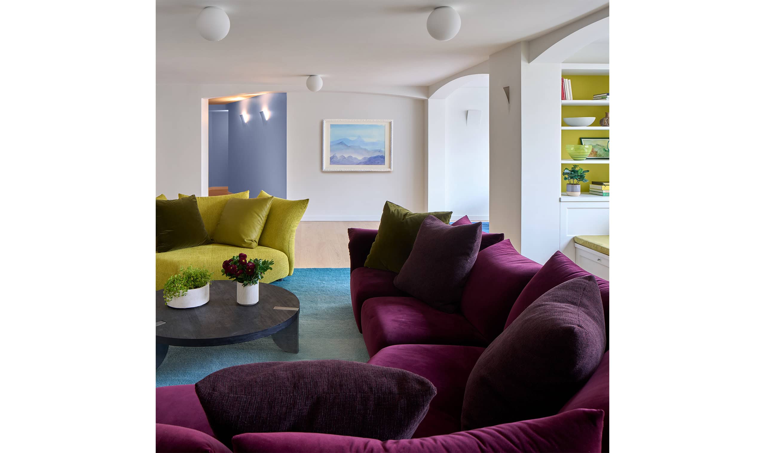 A contemporary living room featuring plush purple and green sofas, a round coffee table, and an open-concept layout with bright decor