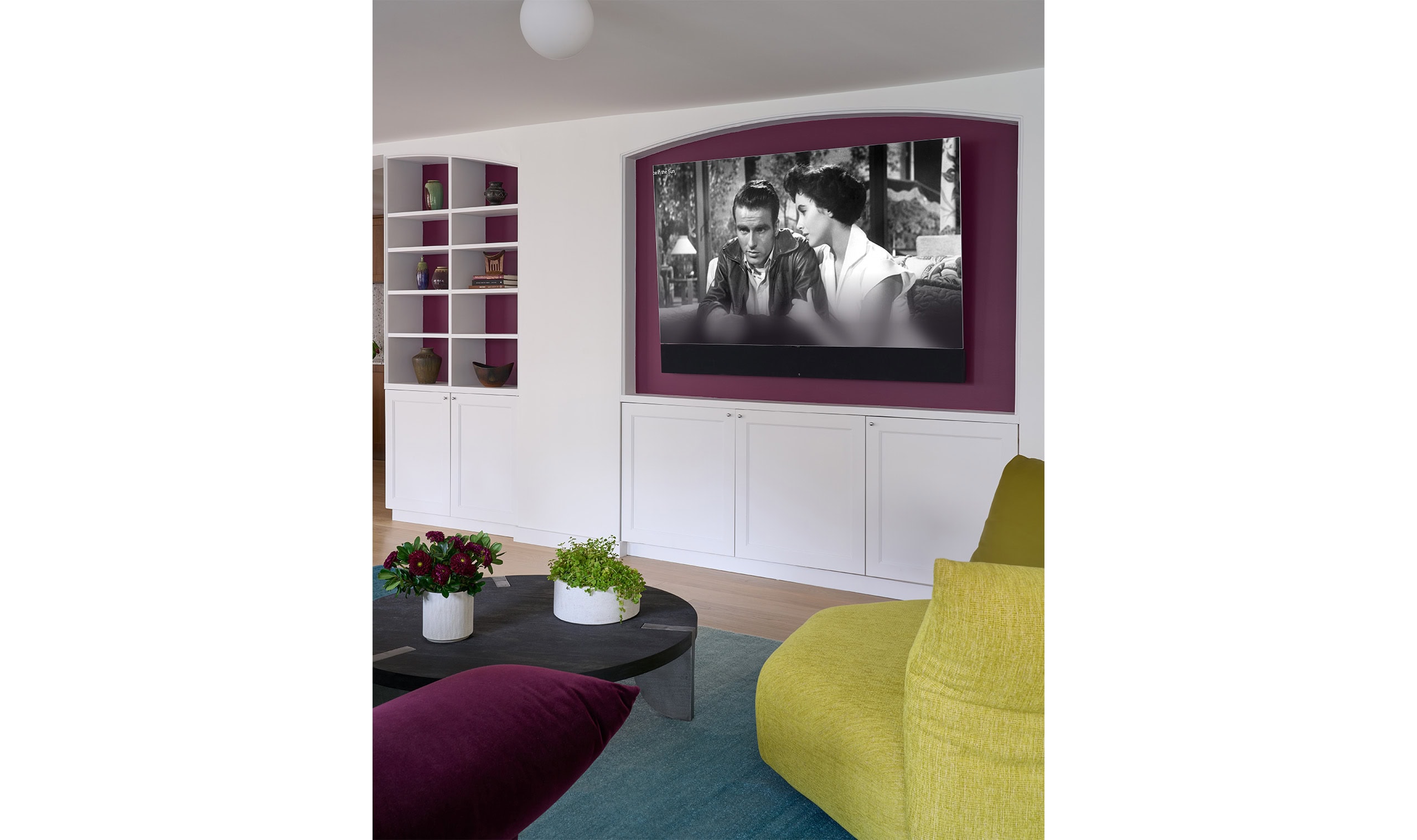 A modern living space with a built-in entertainment system, featuring a black-and-white movie on a recessed screen, vibrant seating, and stylish decor