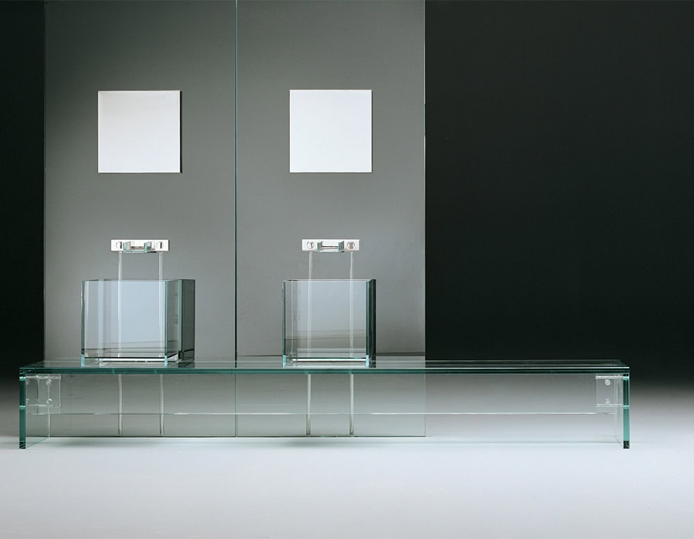 A contemporary bathroom setting featuring two transparent glass sinks with minimalist faucets, set against a sleek, modern backdrop with soft lighting